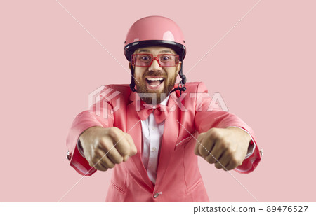 Funny man in pink protective helmet pretends to be motorcycle rider isolated on pink background. Funny man in pink protective helmet pretends to be motorcycle rider isolated on pink background. 89476527