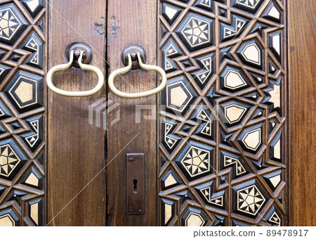 Closeup of two golden ring door knobs over an aged decorated wooden door Closeup of two golden ring door knobs over an aged decorated wooden door 89478917