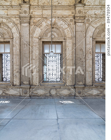 Three adjacent arched windows with decorated iron grid over white marble decorated wall Three adjacent arched windows with decorated iron grid over white marble decorated wall 89478934