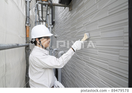 A painter who paints the exterior walls of a detached house with a brush on a scaffold A painter who paints the exterior walls of a detached house with a brush on a scaffold 89479578
