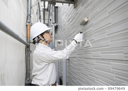 A painter who paints the outer wall of a detached house with a roller on a scaffold A painter who paints the outer wall of a detached house with a roller on a scaffold 89479649