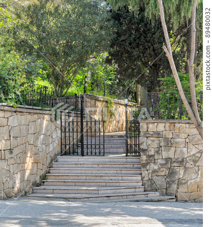 Ascending marble stairs leading to a public park, Stone wall, and fence iron door 89480032