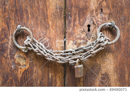 Old rusted padlock, rusted chain, and keyhole on a closed wooden aged grunge door Old rusted padlock, rusted chain, and keyhole on a closed wooden aged grunge door 89480071