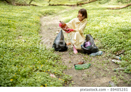 Woman collecting scattered plastic garbage in the woods 89485281