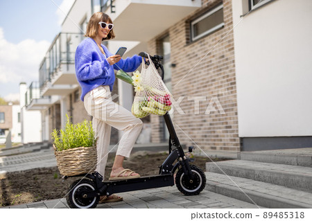Woman going home with fresh vegetables on electrical scooter Woman going home with fresh vegetables on electrical scooter 89485318