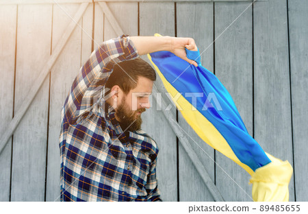 The man in a checkered shirt holds the state flag of Ukraine outdoors in snowy and sunny weather. Ukrainian flag, patriotism. 89485655