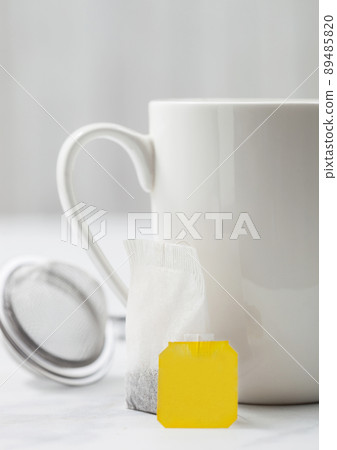 Teabag with yellow blank tag of black tea next to porcelain cup Teabag with yellow blank tag of black tea next to porcelain cup 89485820