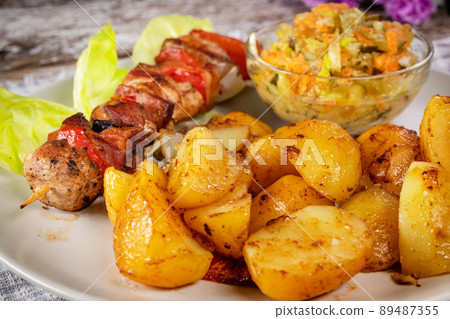 Shish kebab served with roasted potatoes and salad. Shish kebab served with roasted potatoes and salad. 89487355