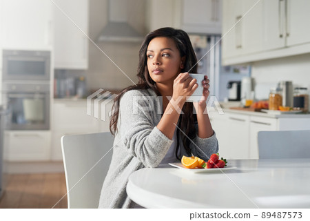 Contemplating the day that lies ahead. Shot of young woman daydreaming while enjoying breakfast in her kitchen at home. Contemplating the day that lies ahead. Shot of young woman daydreaming while enjoying breakfast in her kitchen at home. 89487573