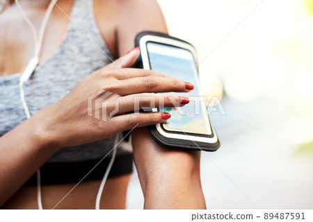 One touch is all it takes to set the rhythm. Shot of an unrecognizable woman listening to music and using her cellphone while exercising outdoors in the city. One touch is all it takes to set the rhythm. Shot of an unrecognizable woman listening to music and using her cellphone while exercising outdoors in the city. 89487591