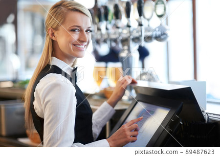 I am a whiz on this till. Beautiful barmaid standing by a till smiling as she rings through a round of drinks. 89487623