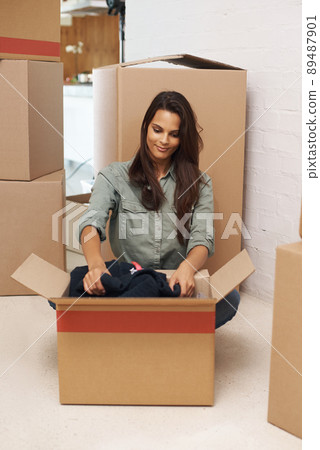 And so, the unpacking begins. A beautiful young woman sitting on the floor in her new house and unpacking boxes. 89487901