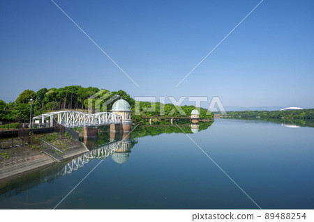 Lake Tama in the fresh green Sayama Hills, the intake tower seen from the weir body and the reflected lake surface 89488254