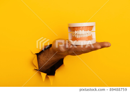 Hand with a model of jaw out of a hole torn in yellow paper wall 89488759