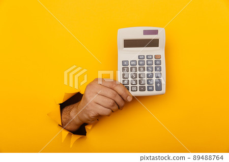 Hand holds calculator through a paper hole in yellow background Hand holds calculator through a paper hole in yellow background 89488764