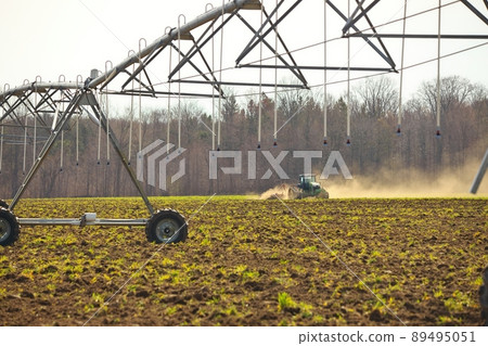 Typical agricultural scene tractor cultivation in field in clouds of dust with irrigation system 89495051