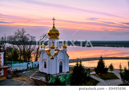 Orthodox church on the territory of the Zaimka tourist complex against the background of a bright sunset over the Ussuri River near the city of Khabarovsk. Russia. 89495696