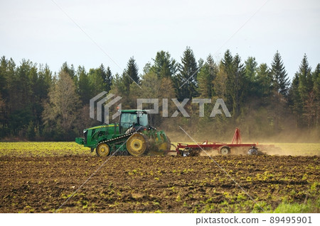 Crawler Tractor plowing ploughing field with Harrow in Spring on Farm with Dust Clouds 89495901