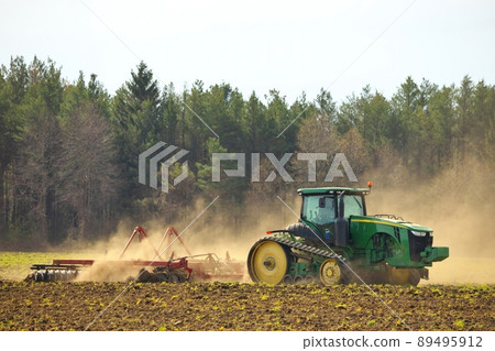 Crawler Tractor plowing ploughing field with Harrow in Spring on Farm with Dust Clouds 89495912