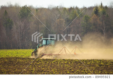 Crawler Tractor plowing ploughing field with Harrow in Spring on Farm with Dust Clouds 89495921