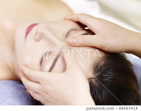 close-up of beautiful young asian woman receiving face massage in spa salon, eyes closed 89497414