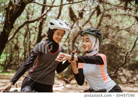 Two woman cycling and her friend looking at the watch 89497590