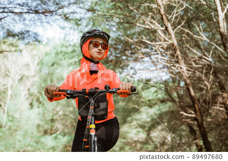 woman in red jacket cycling with trees in the background 89497680