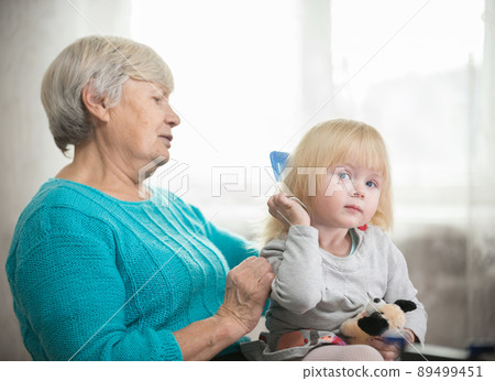 Grandmother combing blonde hair to her little granddaughter Grandmother combing blonde hair to her little granddaughter 89499451