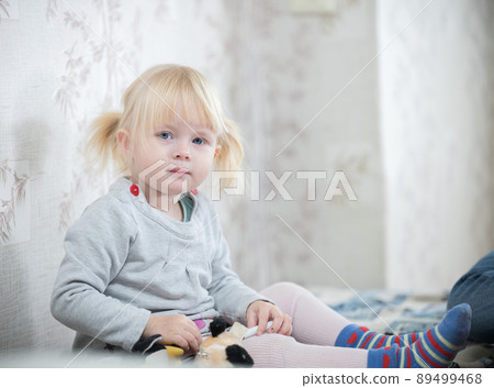 A little blonde baby girl sitting on the bed A little blonde baby girl sitting on the bed 89499468