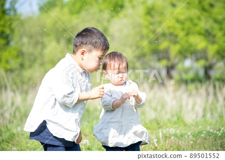 A 5-year-old boy and a 1-year-old girl blowing dandelion fluff 89501552