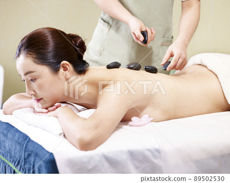 beautiful young asian woman lying on front on bed receiving a hot stone massage in spa salon 89502530