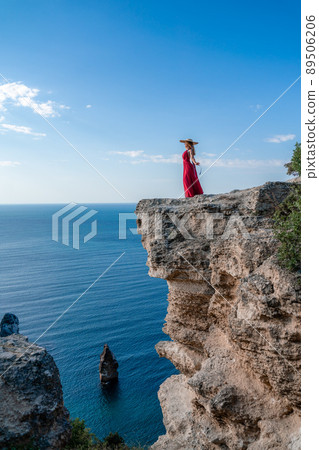 A woman in a red flying dress fluttering in the wind, against the backdrop of the sea. A woman in a red flying dress fluttering in the wind, against the backdrop of the sea. 89506206