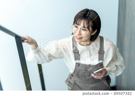 A woman with glasses climbing the stairs with her smartphone 89507382