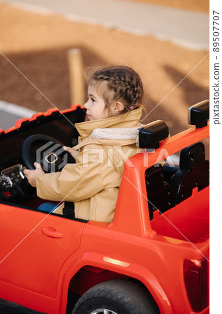 Cute little girl rides in a mini city on a red electric car jeep. Adorable little girl road in toy city. Plays for entertaiment 89507707