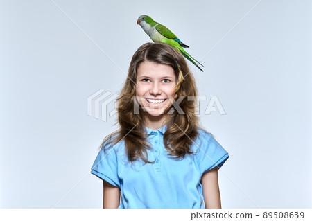 Child girl with pet green quaker parrot looking at camera on light studio background Child girl with pet green quaker parrot looking at camera on light studio background 89508639