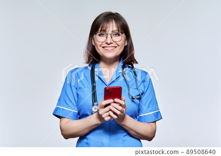 Portrait of female nurse with smartphone in hands, looking at camera on light background Portrait of female nurse with smartphone in hands, looking at camera on light background 89508640