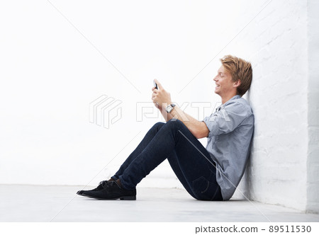 Sending an sms. A young man sitting in the studio and using his cellphone. Sending an sms. A young man sitting in the studio and using his cellphone. 89511530