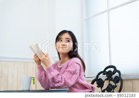 年輕女子在靠窗的座位上看書 89512183