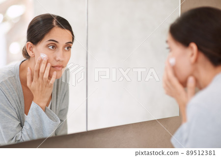 Taking good care of her skin. Shot of a beautiful woman applying moisturizer to her face. 89512381