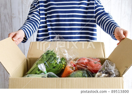 A woman opening a box full of vegetables 89513800