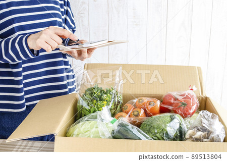 A woman opening a box full of vegetables 89513804