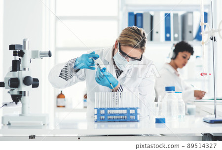 Cropped shot of an attractive young female scientist transferring a liquid sample from a dropper into test tubes in a laboratory with her colleague in the background Cropped shot of an attractive young female scientist transferring a liquid sample from a dropper into test tubes in a laboratory with her colleague in the background 89514327