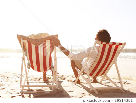 Basking in the warmth together. Rear view of a couple sitting in deck chairs on the beach together. Basking in the warmth together. Rear view of a couple sitting in deck chairs on the beach together. 89514391