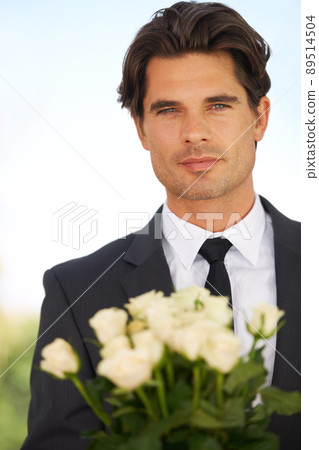A peace offering. Portrait of a handsome young man wearing a suit and holding a bunch of roses. A peace offering. Portrait of a handsome young man wearing a suit and holding a bunch of roses. 89514504