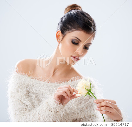 Experience natural beauty. A young woman sitting in a studio holding a white rose. 89514717