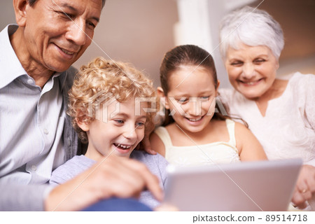Kids with grandparents. A shot of two kids and their grandparents using a digital tablet while sitting on the sofa. 89514718