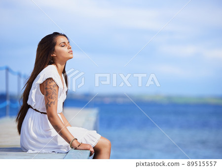 Quiet contemplations beside the sea. Cropped shot of a gorgeous tattooed young woman sitting on a pier. 89515557