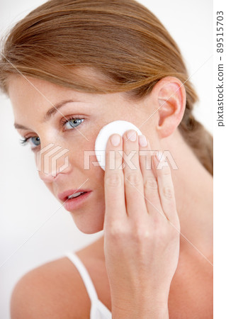 Skincare and beauty. A lovely young woman applying makeup to her cheek with a cotton pad. Skincare and beauty. A lovely young woman applying makeup to her cheek with a cotton pad. 89515703