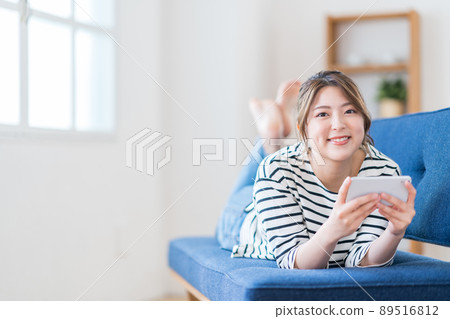 一名年輕女子在沙發上玩智能手機。 一名年輕女子在沙發上玩智能手機。 89516812