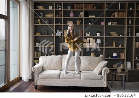 Cheerful excited senior lady dancing to music on home couch Cheerful excited senior lady dancing to music on home couch 89518164